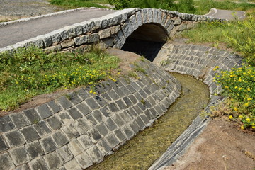 An artificial brook in the park with tiled banks and a bridge