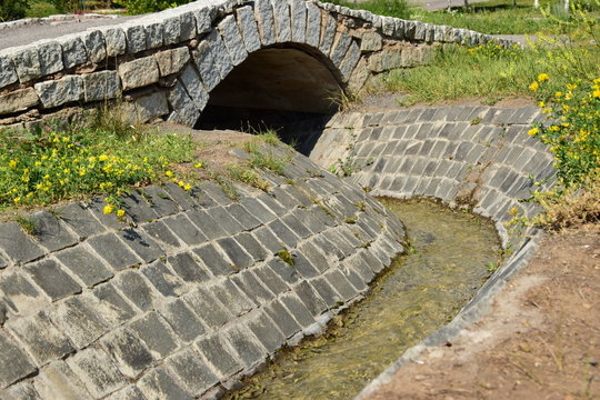An artificial brook in the park with tiled banks and a bridge