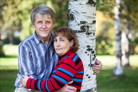 Embracing mature husband and wife standing next to tree in park