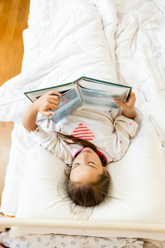 little girl lying at bed in morning and reading big book