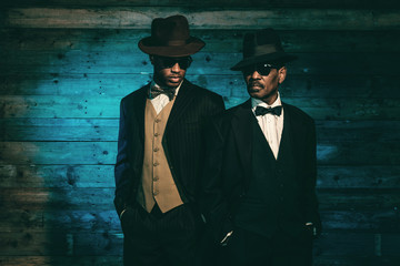 Two vintage african american gangsters in front of old wooden wa