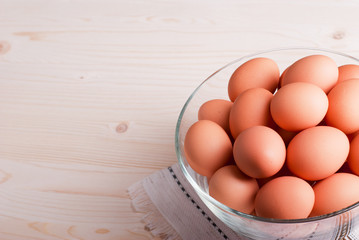 brown eggs in a large glass bowl on a light wooden table view