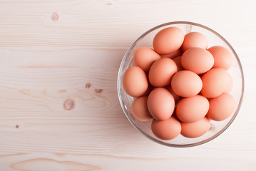 brown eggs in a large glass bowl on a light wooden table view