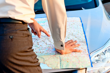 Businessman looking at a map spread out on the hood of a car