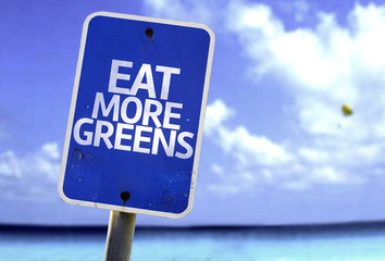 Eat More Greens sign with a beach on background