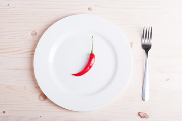 one pepper chilli on a white plate beside the plug on a light wo