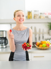 Young woman eating strawberry in kitchen