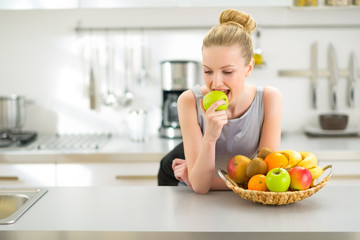 Portrait of young woman eating apple in kitchen