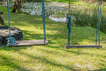 wood playground swing hanging in green grass field.