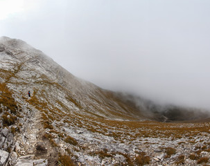 Backpacker walking mountain slope trail in fog. 