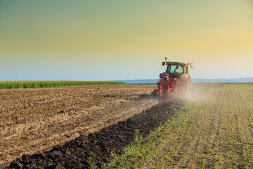 Naklejka premium Farmer plowing stubble field with red tractor