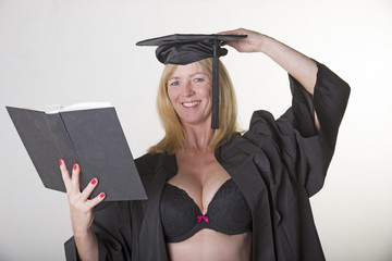 Mature female student in cap and gown reading a book