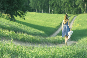 girl walking along the road in a field alone - obrazy, fototapety, plakaty