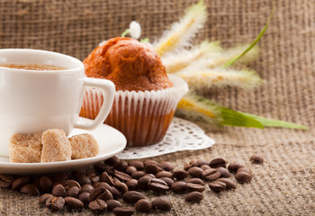 cup of coffee with cake and coffee beans on burlap tablecloth