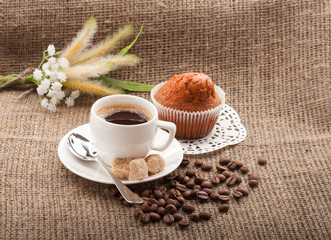 cup of coffee with cake and coffee beans on burlap tablecloth
