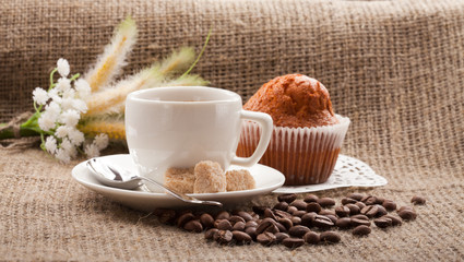 cup of coffee with cake and coffee beans on burlap tablecloth