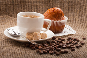 cup of coffee with cake and coffee beans on burlap tablecloth