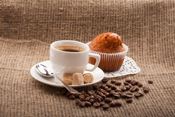 cup of coffee with cake and coffee beans on burlap tablecloth