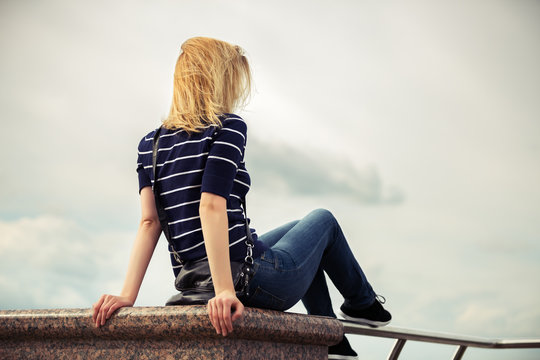 Young fashion woman sitting against a cloudy sky