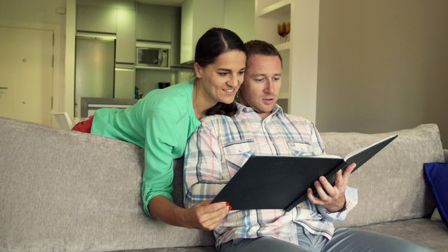 Young couple watching photos in album on sofa at home