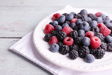 Iced berries on plate, on color wooden background