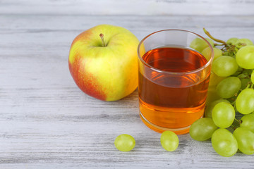 glass of juice with fresh grape and apple on grey wooden table