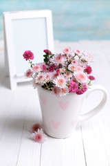 Beautiful flowers in cup on table on light blue background © Africa Studio