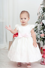 Little girl in a white dress  stand near a Christmas fir-tree