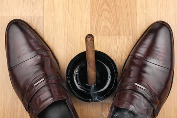 Classic men's shoes, ashtray and  fuming cigar on the wooden flo