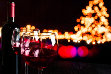 red wine glass near bottle against bokeh lights background