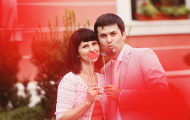 Young parents having fun with mustache and lips made of paper
