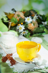 cup of tea with sugar candy and a bouquet of flowers in the back