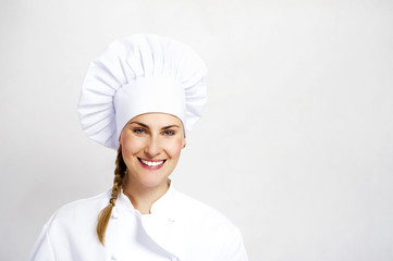 A young, female chef in a traditional hat and coat.