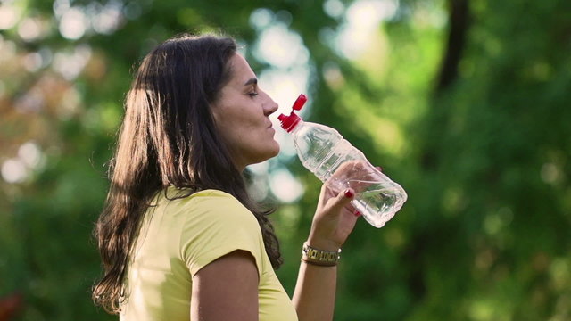 Sporty woman drinking water in park, slow motion, steadycam