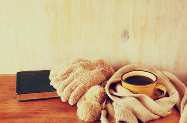 Cup of black coffee with a warm scarf and old book on wooden bac