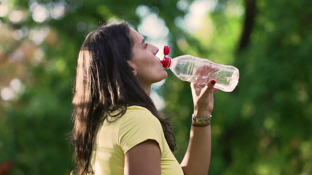 Sporty woman drinking water in park, slow motion shot, steadycam