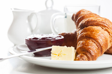 Croissants with butter and a glass of milk on a plate