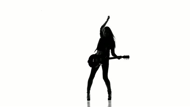 Silhouette of a young girl dancing with electric guitar on a