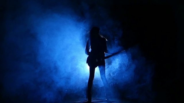 Silhouette of a young girl playing on electric guitar. Slow