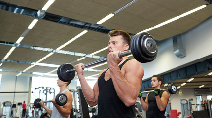 group of men flexing muscles with barbell in gym