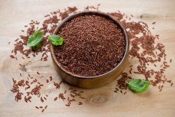 Raw red rice kernels in a wooden bowl, horizontal shot