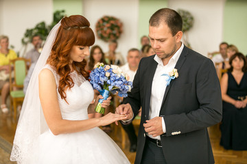 handsome groom putting wedding ring on brides hand at registry o