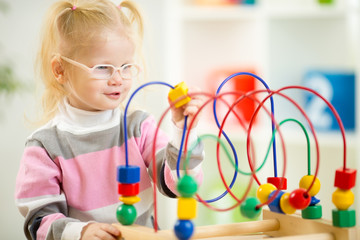 Kid in eyeglases playing colorful toy in home interior