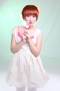 Girl with red hair with lollipop in white dress on light