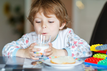Obraz na płótnie Canvas Little kid boy drinking milk and playing with construction block
