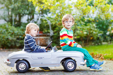 Two happy twins playing with big old toy car in summer garden, o