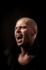 Handsome young man screams into a dark copy space as a sign of f