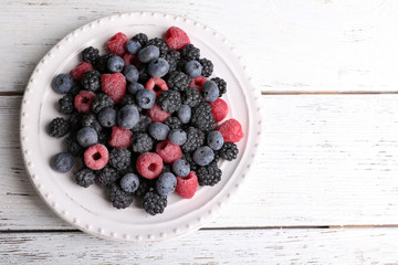 Iced berries on plate, on color wooden background