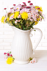 Beautiful flowers in pitcher on table on light background