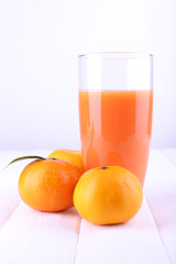 Glass of juice and ripe sweet tangerine on white wooden table